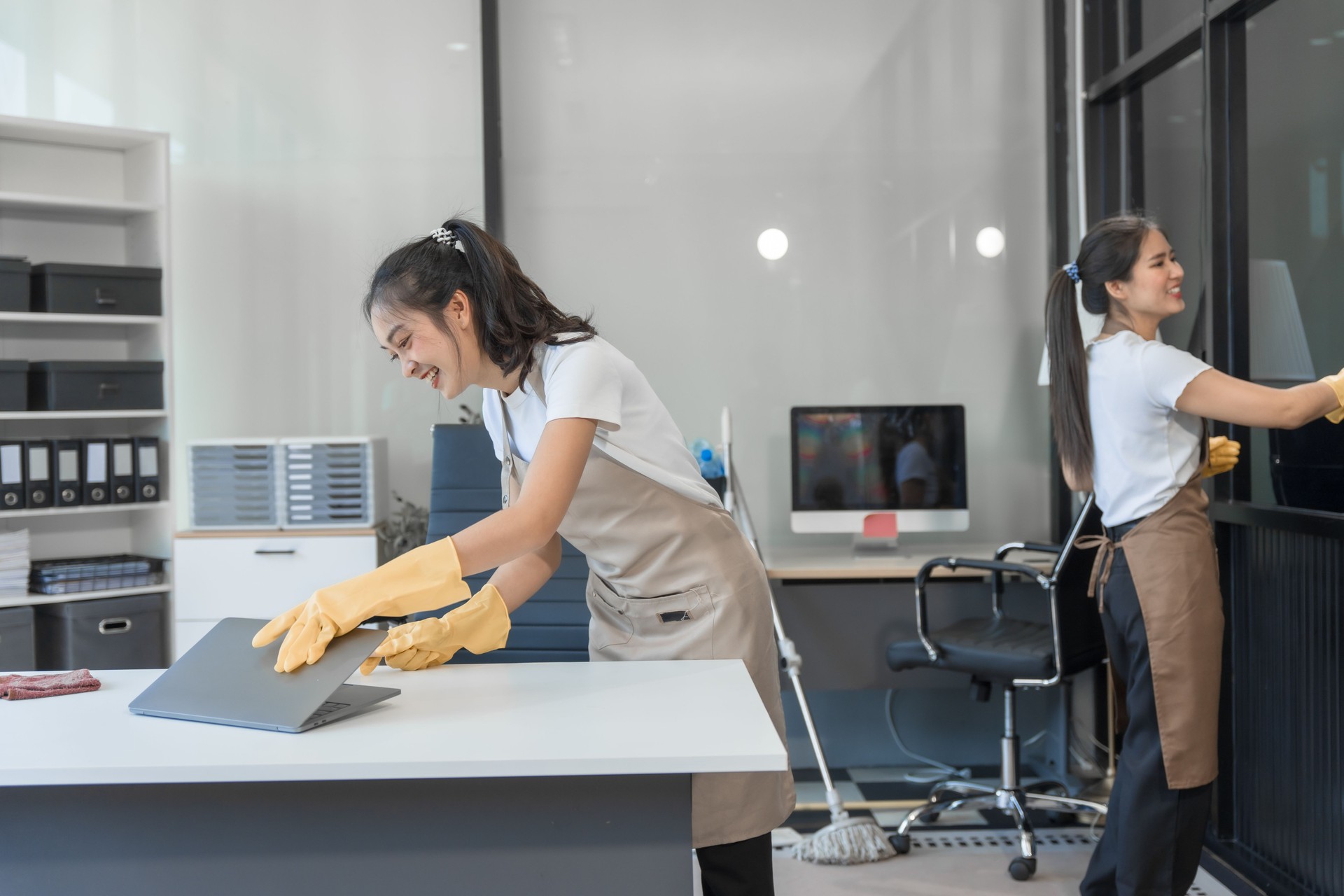 Two Asian housekeepers wear overalls and work together efficiently to clean the living room, study, office.They wipe the windows, mop the floors, inspect the shop to make sure the work is spotless
