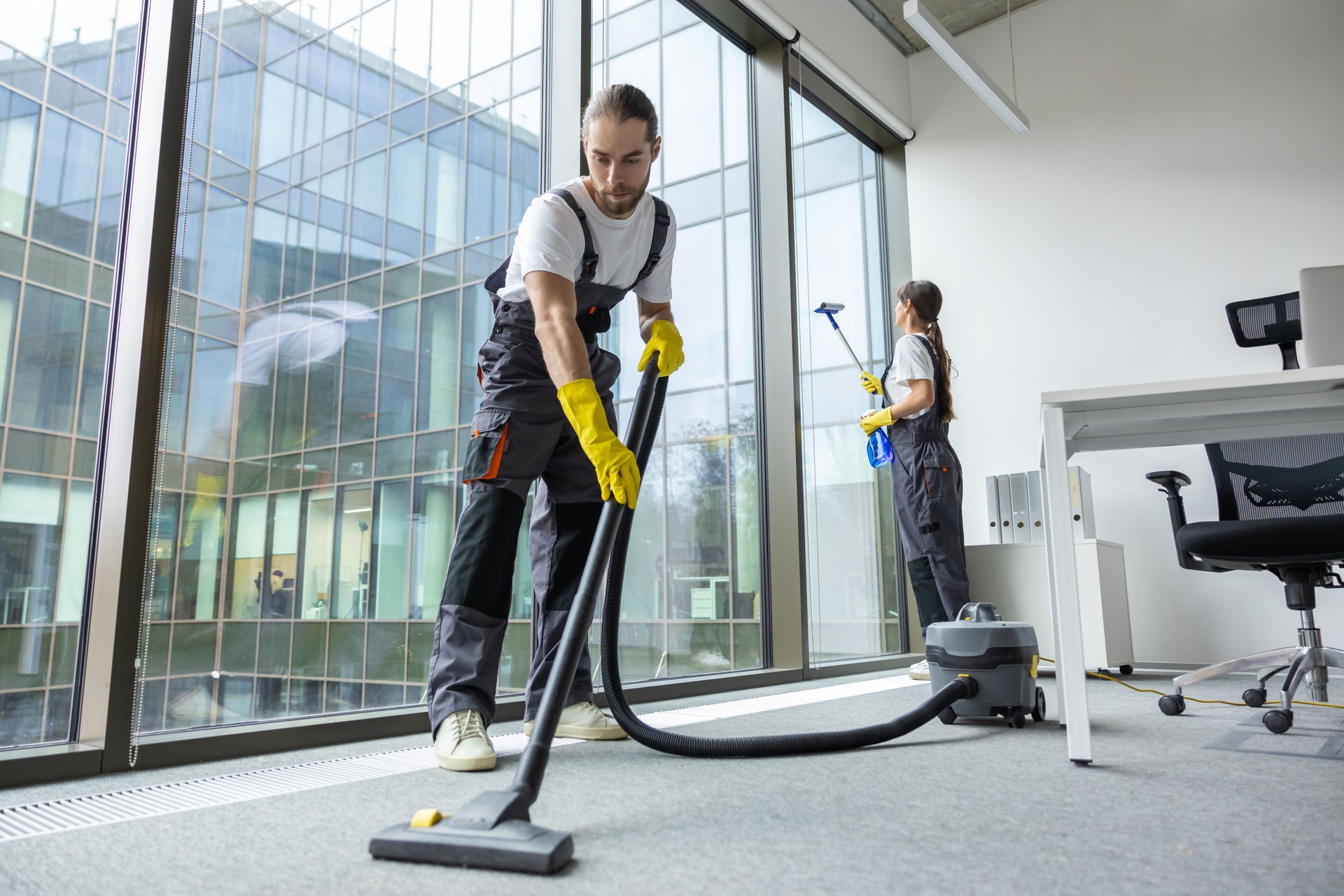 Young man in uniform vacuum cleaning the floor in the conference room